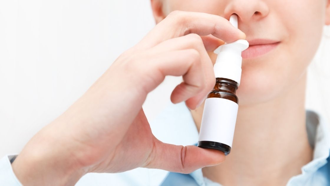 Woman holding nasal spray towards nostrils.