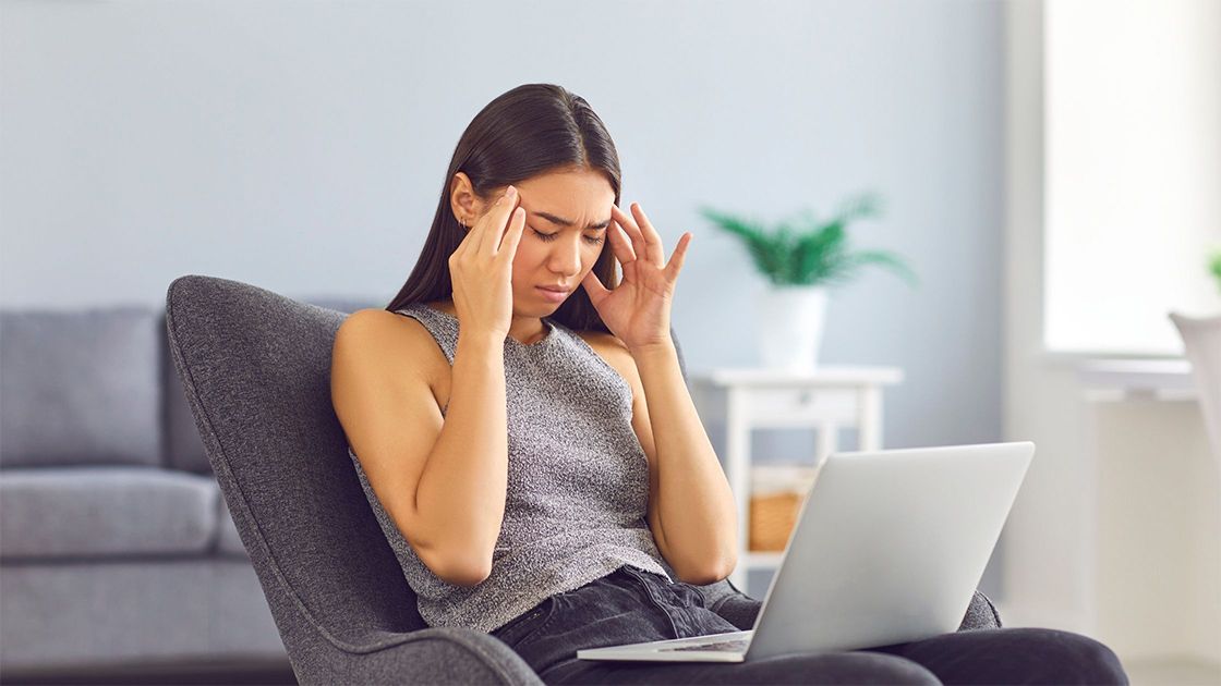 Lady holding her temples, with a laptop.
