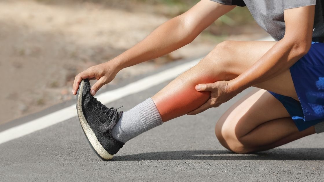 Man holding left leg wearing gray running shoes.