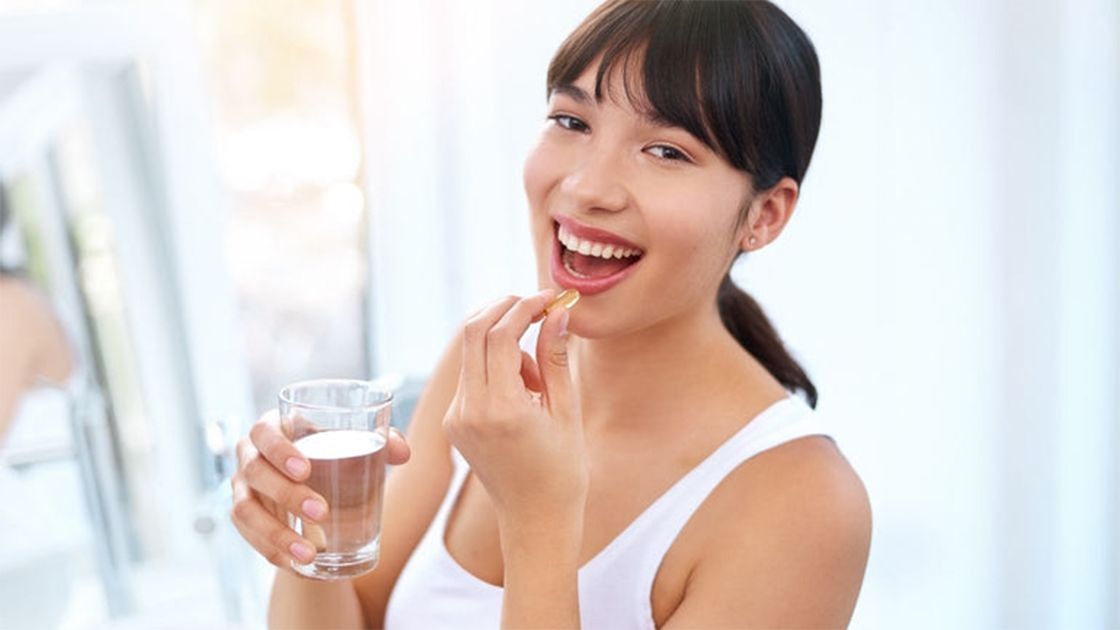 Woman wearing a white sando taking a vitamin pill, smiling.