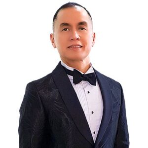 Man wearing tuxedo suit, smiling facing camera.